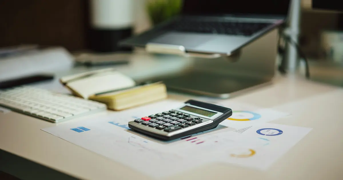 Calculator on printed budget charts beside a laptop, estimating how much a website costs