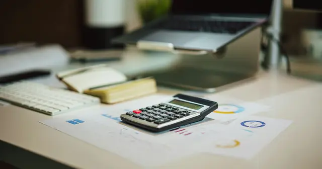 Calculator on printed budget charts beside a laptop, estimating how much a website costs